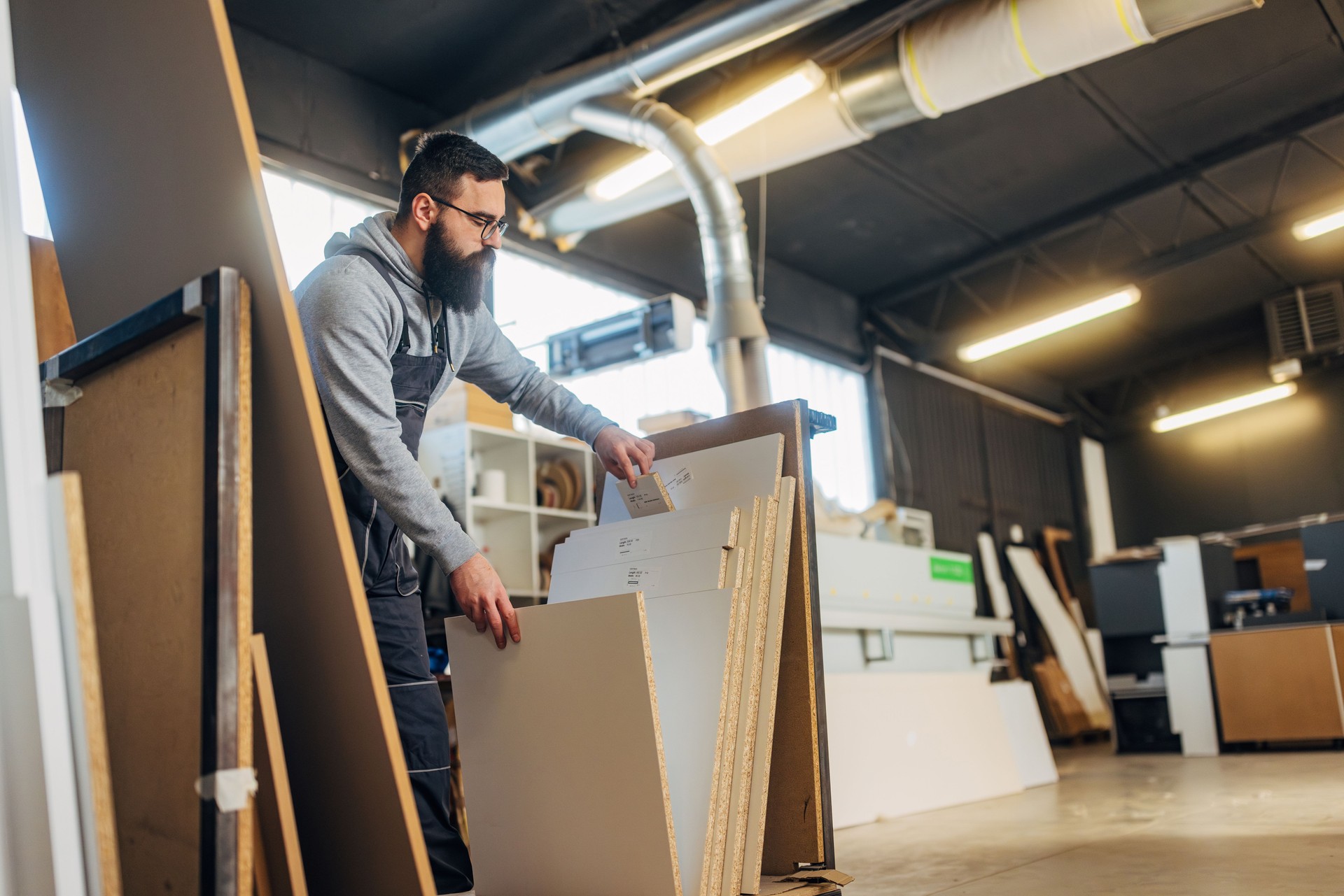 A bearded worker in a large workshop makes furniture from wood